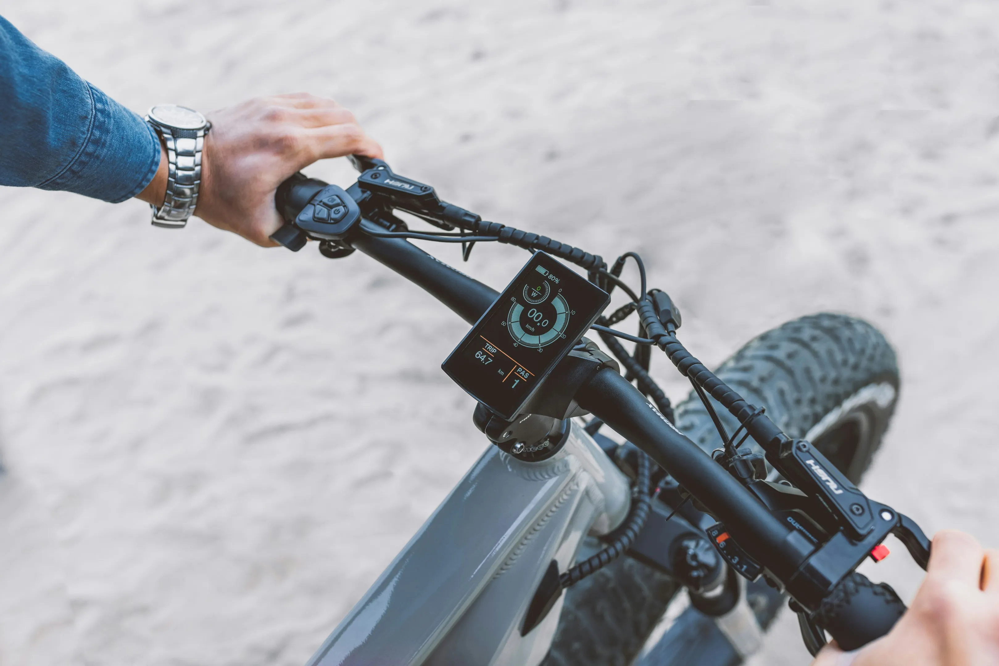A cyclist's hands on the handlebars of an e-bike, with a digital speed display mounted on the stem