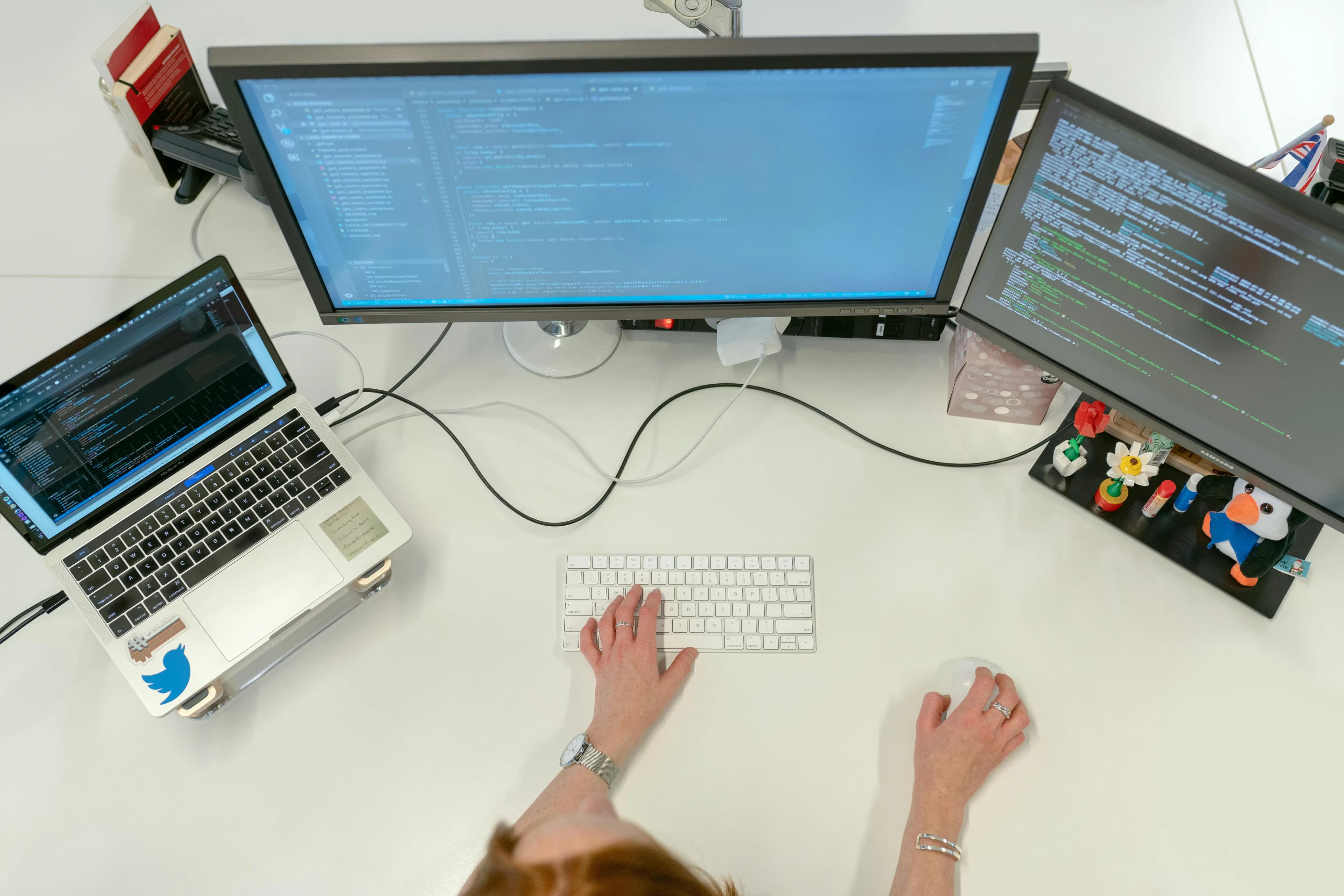 An overhead view of a developer's desk with three screens full of code, a keyboard and a mouse