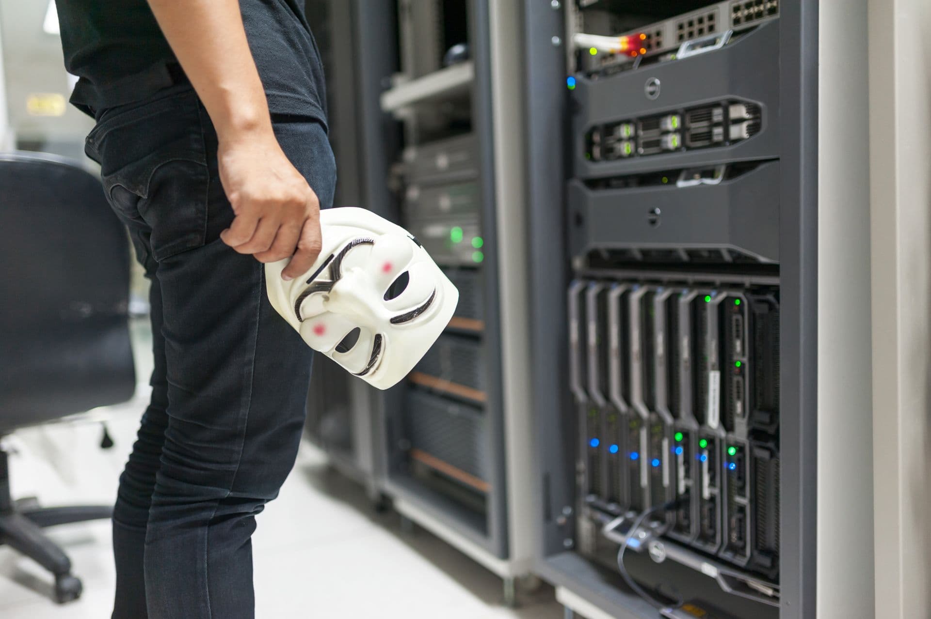 A person holding a Guy Fawkes mask in front of server racks